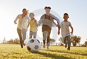 Young family chasing after a football in a park