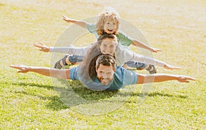 Young family with child having fun in nature. Fly concept, little boy is sitting pickaback while imitating the flight.