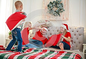 Young family with children having fun at home fighting pillows on bed in christmas, happy lifestyle on holidays parents with kids