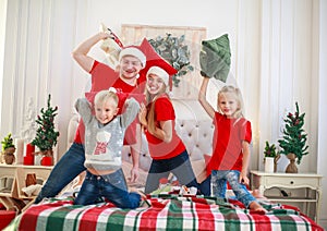 Young family with children having fun at home fighting pillows on bed in christmas, happy lifestyle on holidays parents with kids