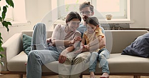 Young family couple with little daughter cuddle on couch