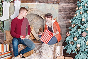 Young family couple looking at gifts on the fireplace near New Year tree