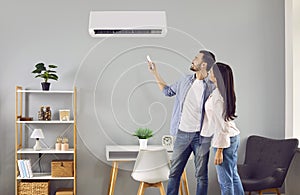 Young family couple setting up the temperature on a modern air conditioner at home