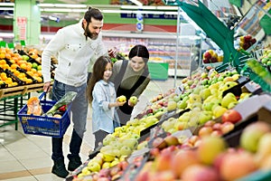 A young family with a daughter choose apples in the vegetable Department in the supermarket.