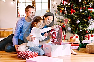 Young family with daughter at Christmas tree at home.