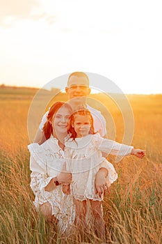 Young family with daughter sits on meadow among grass at sunset