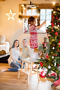 Young family with daugter at Christmas tree at home.