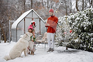 Young family with a dog at snowy backyard during winter holidays
