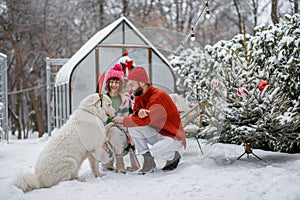 Young family with a dog at snowy backyard during winter holidays