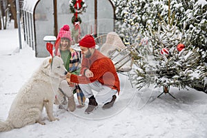 Young family with a dog at snowy backyard during winter holidays