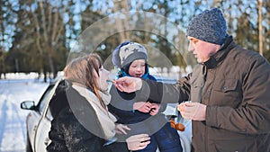 A young family is eating tangerines during a picnic on a winter day.