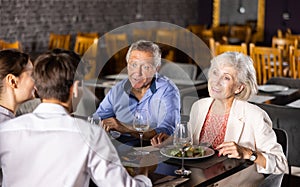 Young family and elderly couple of spouses eating in cafe celebrating event and communicating