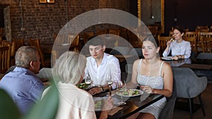 Young family and elderly couple of spouses eating in cafe celebrating event and communicating