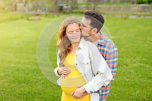 Young family is expecting a baby. Happy couple of parents-to-be walking together. Handsome man hugging and kissing of pregnant