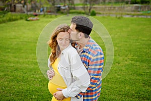 Young family is expecting a baby. Happy couple of parents-to-be walking together. Husband embracing wife gently and holding her