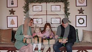 A young family of four unpacks their Christmas gifts together in a New Year's Eve atmosphere