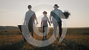 Young family having fun outdoors in their farm. Gardener woman pushing wheelbarrow with vegetables at sunset. Family