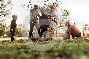 Young family having fun in a park throwing autumn leaves
