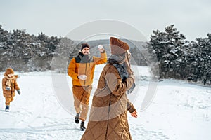 Young family having fun in winter snowy forest