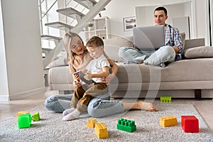 Young family at home, mom and kid watching video on tablet, dad working on pc.