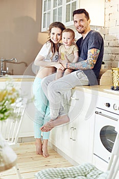 Young family at home in the morning on a day off. Married couple and their little baby baby in her arms. Joyful and happy faces