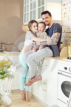 Young family at home in the morning on a day off. Married couple and their little baby baby in her arms. Joyful and happy faces