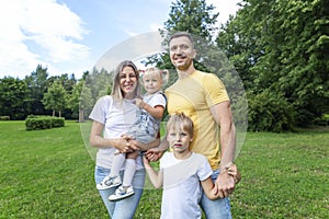 A young family in jeans and white T-shirts plays with small children in a green summer park on a sunny day