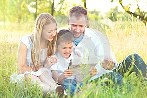 Young family with kid using tablet PC in summer park