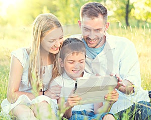 Young family with kid using tablet PC in summer park