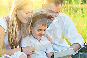 Young family with kid using tablet pc in summer park