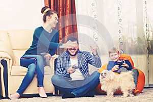Young family with little boy and small dog having fun spending quality time together playing video games at home due to isolation