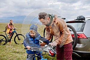 Young family with little children preparing for bicycle ride in nature, putting off bicycles from car racks. Healthy