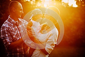 Young family with little daughter walking in the park at sunset