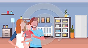 Young family loving parents holding little son at home baby bed newborn room wooden crib kid bedroom interior cartoon