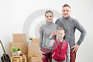 Young family, man woman and child son in new apartments. The child holds the keys to the apartment. Boxes with cargo on