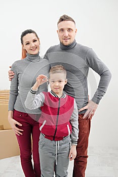 Young family, man woman and child son in new apartments. The child holds the keys to the apartment. Boxes with cargo on