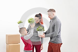 Young family, man woman and child son in new apartments. They are holding green potted plants. Boxes with cargo on a