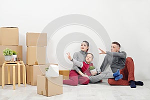 Young family, man woman and child son sits at floor in new apartments. Boxes with cargo on a white background.