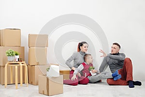 Young family, man woman and child son sits at floor in new apartments. Boxes with cargo on a white background.