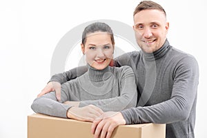 A young family, a man and a woman in gray sweaters are moving to a new apartments. Boxes with cargo on a white