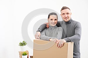 A young family, a man and a woman in gray sweaters are moving to a new apartments. Boxes with cargo on a white