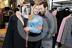 A young family, a man and a woman hug and choose a black coat in a clothing store