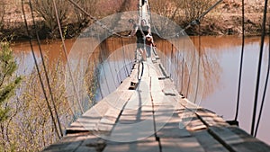 Young family mom, dad and daughter walk on the old suspension bridge over the river.