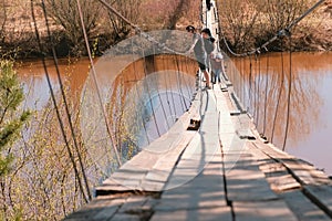 Young family mom, dad and daughter walk on the old suspension bridge over the river.