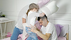 Young family: mom dad and little son are having fun pillow fight on bed.
