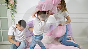 Young family: mom dad and little son are having fun pillow fight on bed.