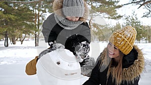 Young family, mom, son and dad are building a snowman in winter city park.