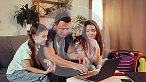 Young family, mother, father and daughter sitting at home with suitcases, planning trip, making online hotel reservation