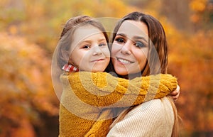 Young family, mother and little son, on walk in autumn forest, mom and child holding hands and walking along path covered with