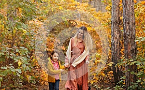 Young family, mother and little son, on walk in autumn forest, mom and child holding hands and walking along path covered with
